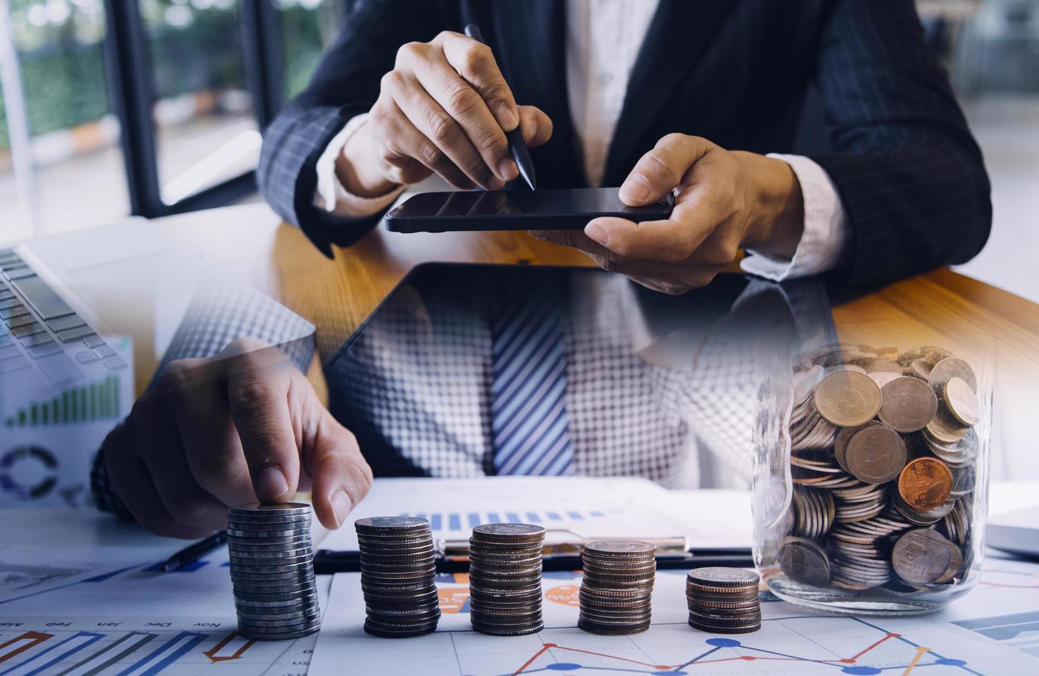 A double exposure image of a businessman using a tablet, financial charts, and stacked coins, symbolizing investment and wealth management.