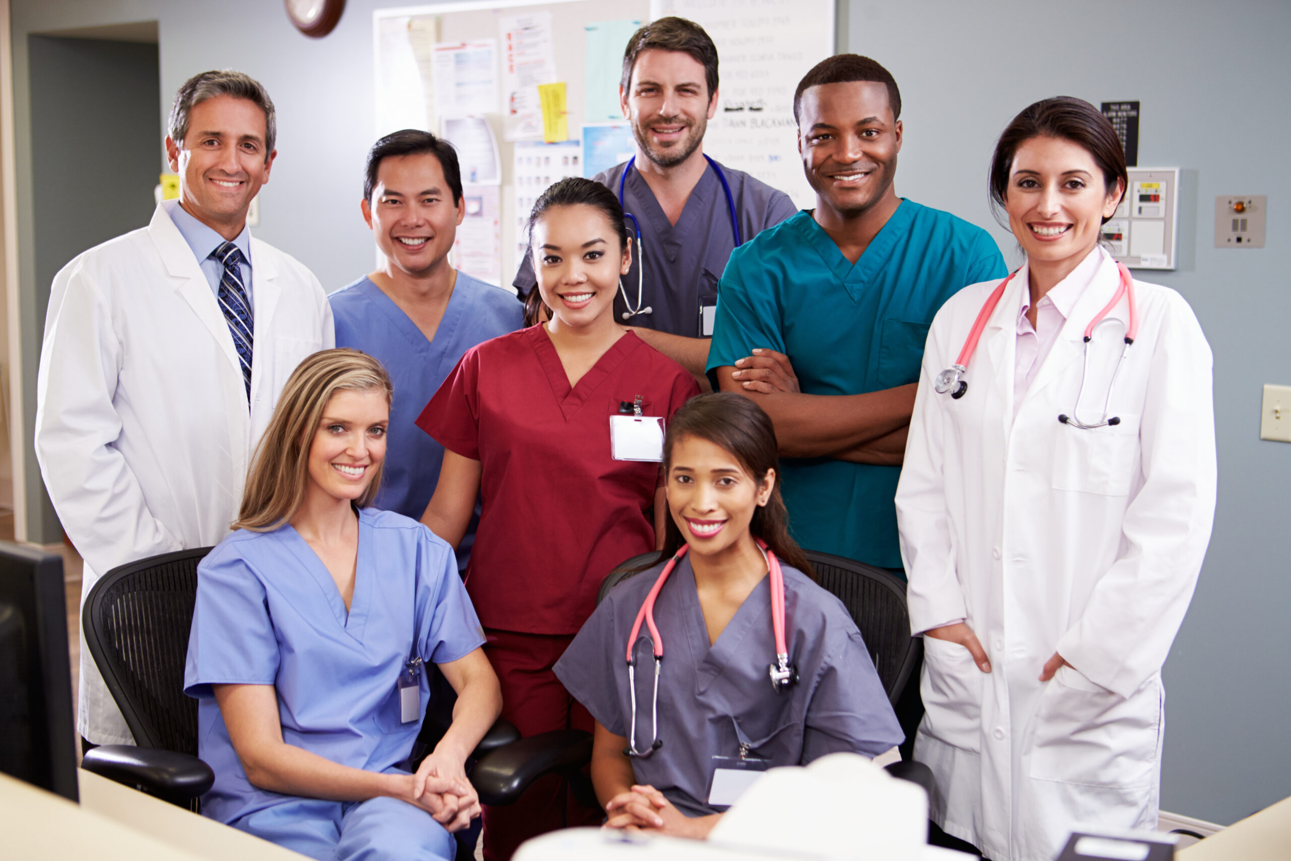 A diverse group of smiling healthcare professionals, including doctors and nurses, posing in a hospital setting.